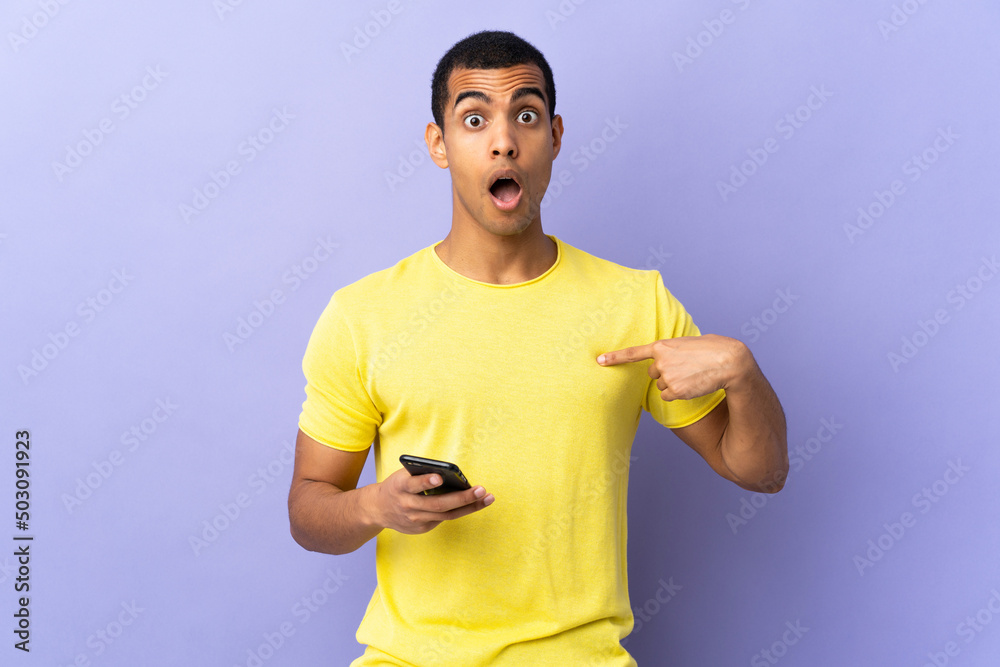 African American man over isolated purple background using mobile phone with surprise facial expression African American man over isolated purple background using mobile phone with surprise facial expression