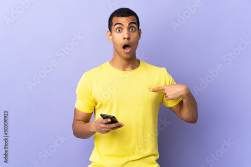 African American man over isolated purple background using mobile phone with surprise facial expression