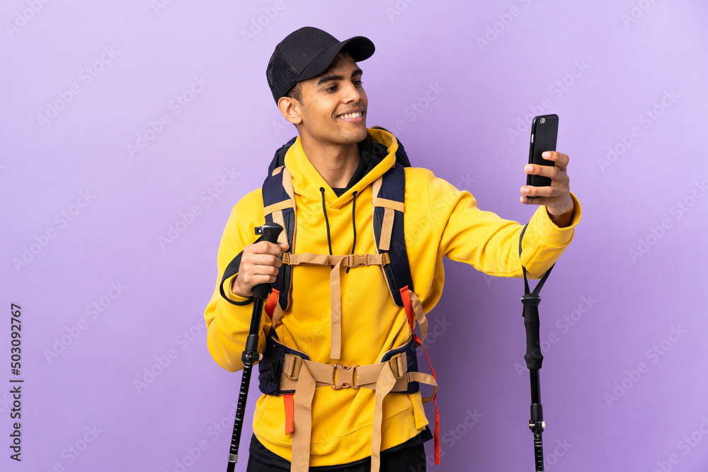 African American man with backpack and trekking poles over isolated background making a selfie
