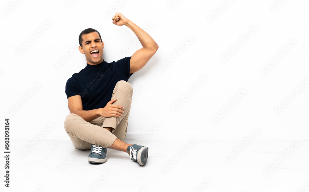 Fototapeta premium African American man sitting on the floor celebrating a victory