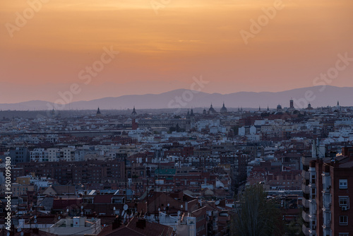 An amazing warm sunset over the skyline of Madrid with views on the mountain range, 
Sierra de Guadarrama on the horizon, seen from las siete tetas on Cerro Tio Pio hill side.