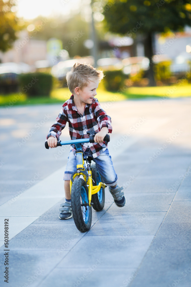 stylish European boy in shirt and jeans rides balance bike on asphalt. Child riding without helmet stylish European boy in shirt and jeans rides balance bike on asphalt. Child riding without helmet