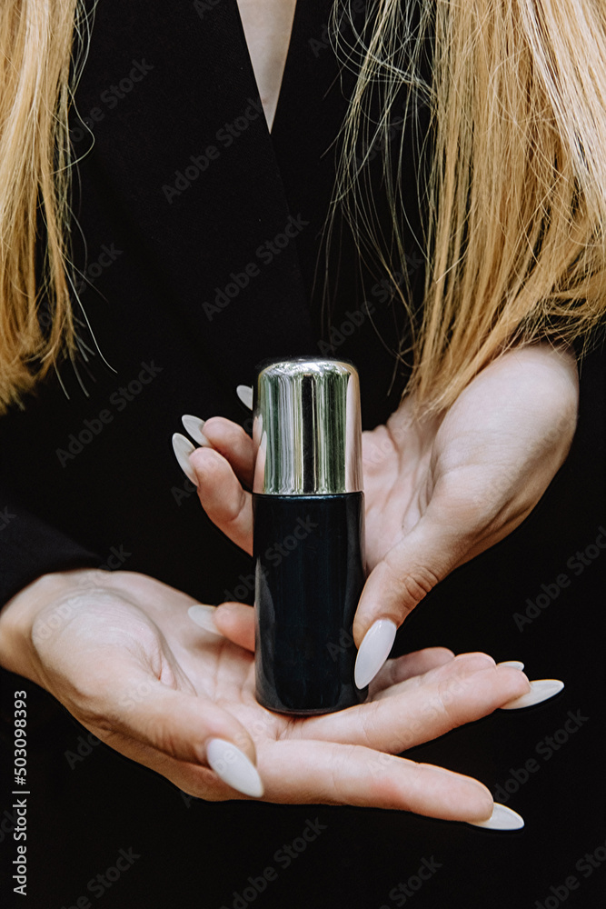Fototapeta premium Black jar with silver lid spray cosmetics in the hands of a girl on a body background