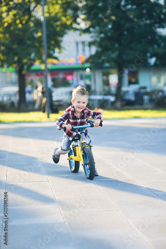 stylish European boy in shirt and jeans rides balance bike on asphalt. Child riding without helmet © natalialeb