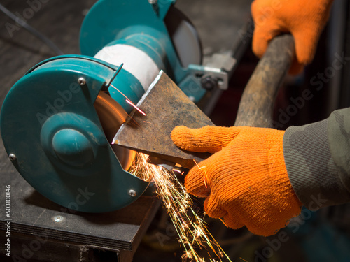 man sharpening an ax blade on a grinder
