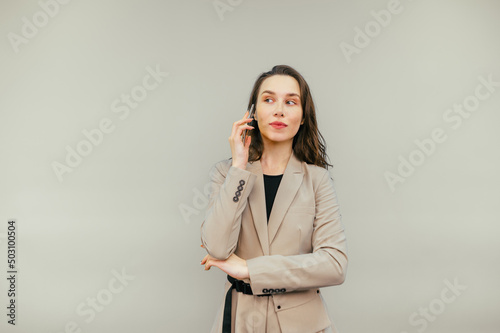 Cute business woman in a jacket talks on the phone with a smile on his face and looks away, isolated on a beige background.