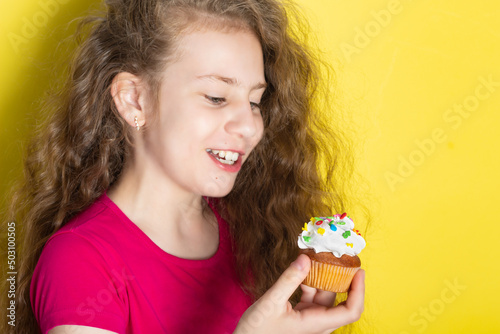 Girl with curly hair  wearing a red shirt  delightedly examining a cupcake she s holding.