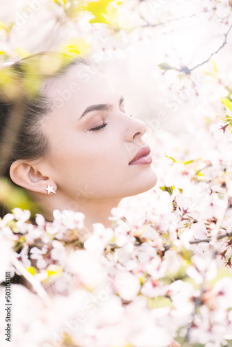 Beauty  lifestyle and nature concept. Beautiful brunette woman portrait in white sakura blossom background during spring time in sunny day. Model with day make-up and closed eyes dreaming