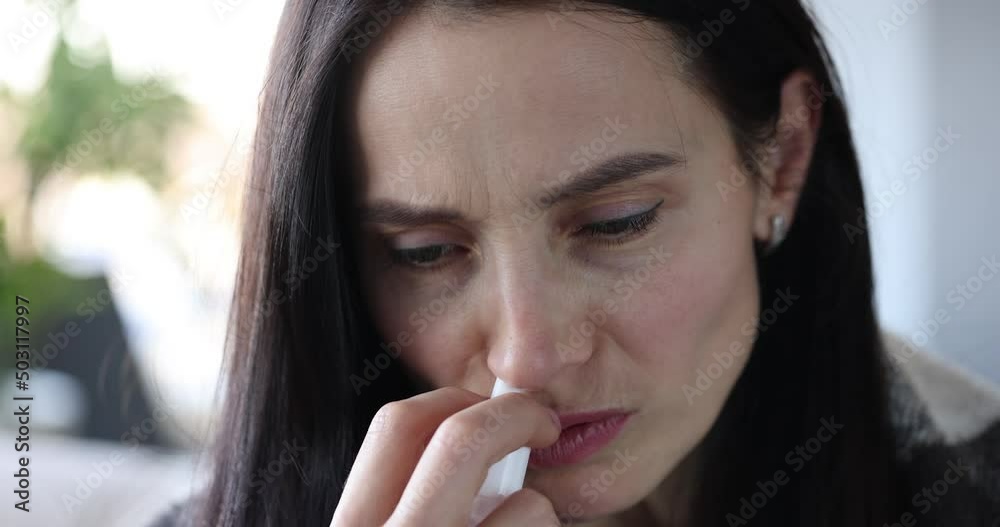 Woman with runny nose holds medicine in hand and puffs into red nose Woman with runny nose holds medicine in hand and puffs into red nose