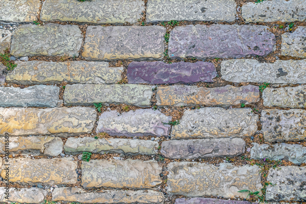 Obraz premium Texture of ancient stone paving stones close-up. Top view of old shabby colorful decorative blocks installed on the road