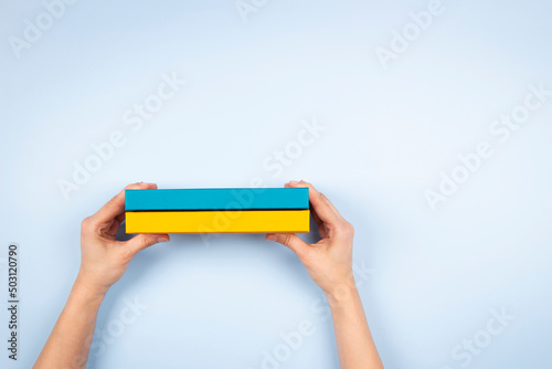 Woman hands holding two blue and yellow color books over light blue background. Education, self-learning, book swap photo