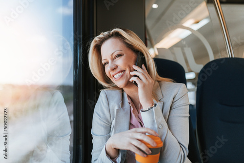 Canvas Print A middle-aged business woman is sitting in the cab of a high-speed train, looking through window and talking on phone