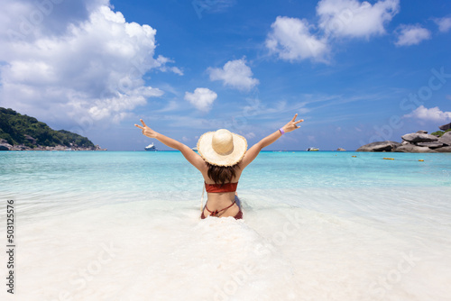 back view of woman wearing a straw hat and orange bikini relax on the beach with beautiful blue sky.at Similan island Phuket Thailand , summer vacation concept