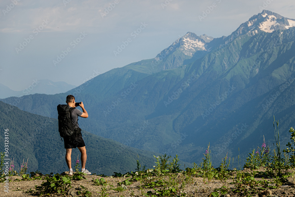 A male hiker with a large backpack photographs a beautiful mountain landscape