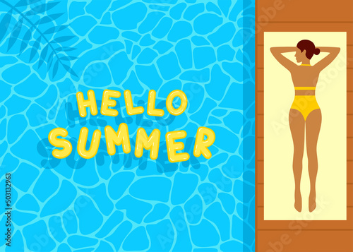 Young woman in a yellow swimsuit lying on a beach towel by the blue pool. Yellow inflatable letters hello summer floating on the water surface