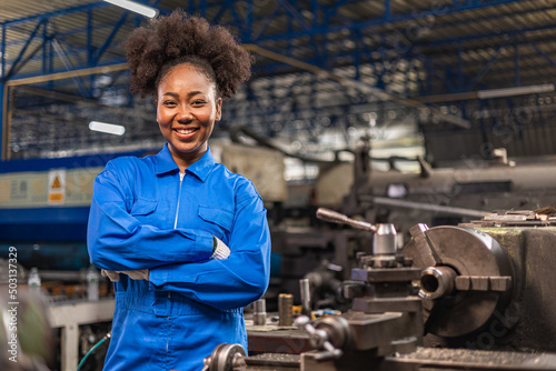 African American Young woman worker  in protective uniform operating machine at factory Industrial.People working in industry.Portrait of Female  Engineer looking camera  at work place. photo