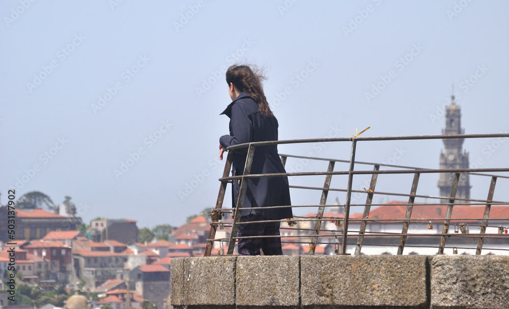 Obraz premium Pessoa do sexo feminino num miradouro da cidade do Porto em Portugal a contemplar as vistas, Torre dos Clérigos em desfoque - serra do pilar, cabelo ao vento, Vila Nova de Gaia