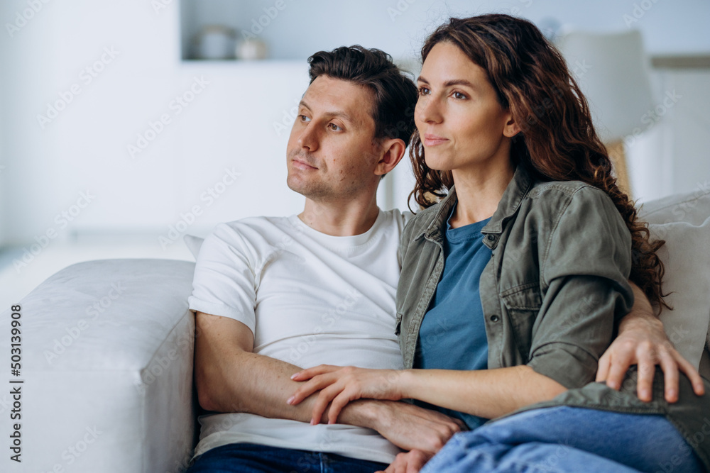 Happy newlyweds with dark hair sit on comfortable sofa in living room and discuss plans for future smiling broadly closeup Happy newlyweds with dark hair sit on comfortable sofa in living room and discuss plans for future smiling broadly closeup