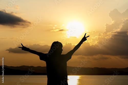 Silhouette of woman standing arms raised in the sunset. Strong female with open arms silhouette in sunrise against sun flare. Carefree person living a free life. Success freedom happy life concept.