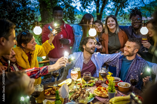 Canvas Print Large group of happy friends singing and having during dinner on balcony, mixed