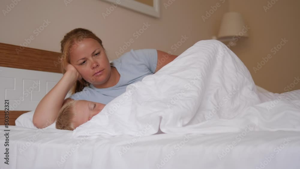 Close-up of a little boy sleeping in bed in the morning, the mother carefully covers the child with a blanket.
