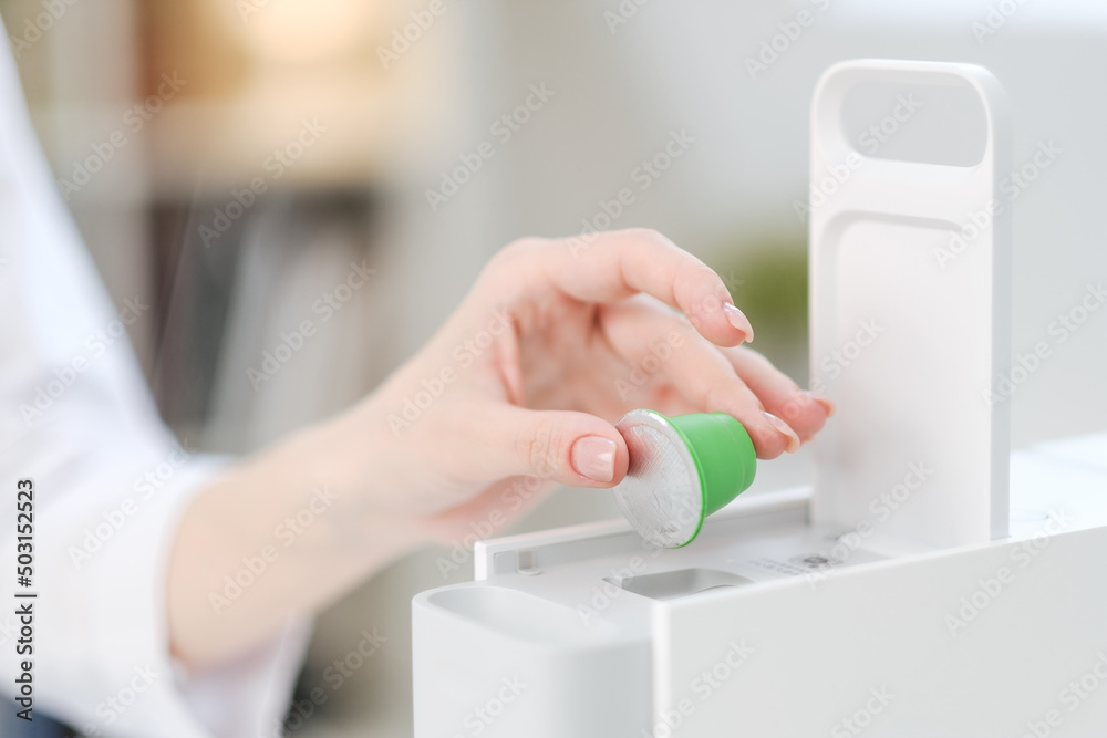 A woman holds coffee capulas in her hands and prepares espresso in a capsule coffee machine. White background. A bright room. A woman holds coffee capulas in her hands and prepares espresso in a capsule coffee machine. White background. A bright room.