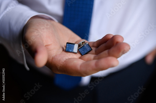 A man in a shirt holds stylish cufflinks in his hands, close-up.