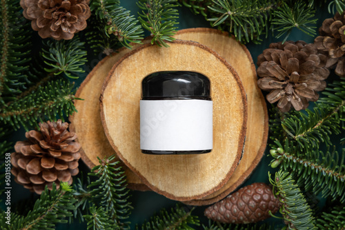 Glass jar between fir branches and pine cones on wooden piece top view. Mockup. photo