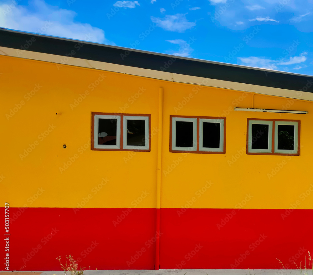 A house painted red and yellow against a background of blue clouds.