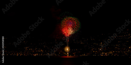 Long exposure of fireworks reflecting in the water above a city in night lights photo