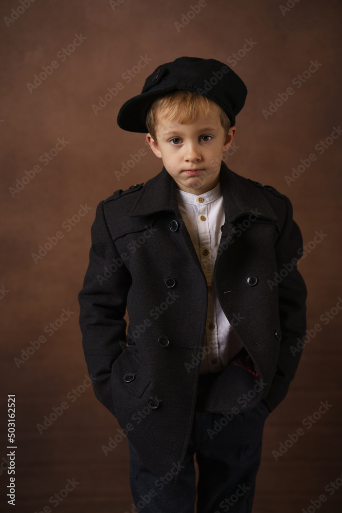 Portrait of a small proud looking boy smartly dressed, standing against a brown background. Retro style.