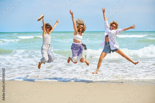 Three laughing women is jumping at beach enjoy enjoying the seaside. Friendship and summer time concept.