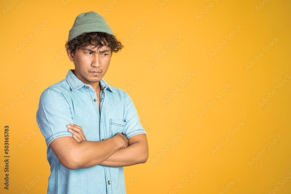 unsure asian young man with arms crossed on isolated background