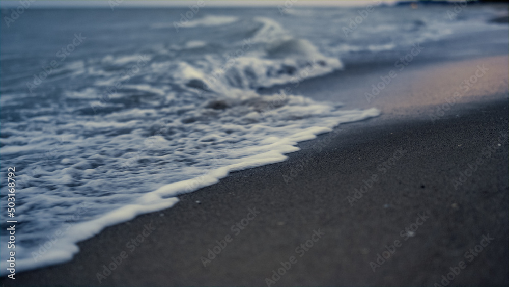 Obraz premium Sea wave crashing sand on sunset evening beach. Dusk ocean tide splash coastline