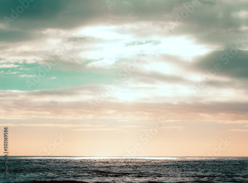 Atardecer en la playa con luz del sol bajando entre las nubes © Richard