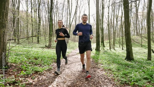wide slow motion 4k shot of man and woman running in the woods. Trail runners in forest. Sport and wellness concept