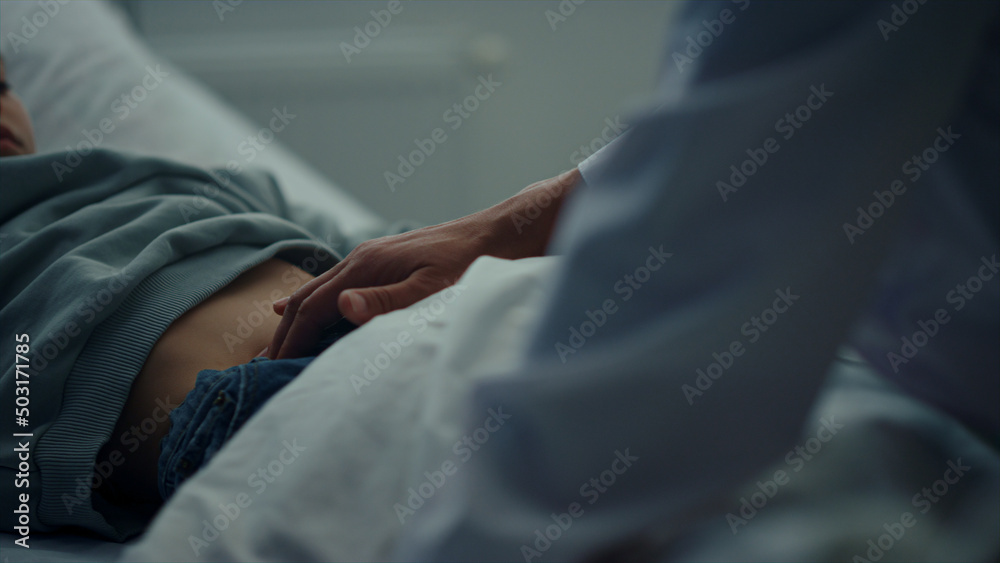 Doctor touching patient stomach in emergency ward closeup. Sick kid lying in bed