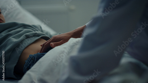 Doctor touching patient stomach in emergency ward closeup. Sick kid lying in bed