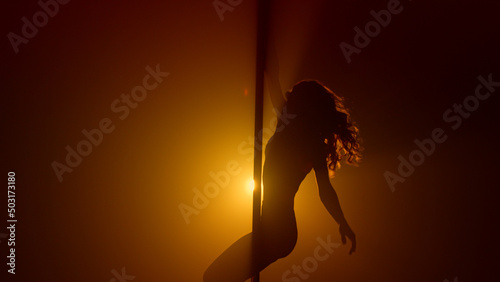 Woman silhouette practicing poledance in club. Sexual lady turning round pole. photo