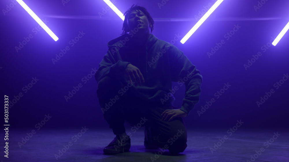 Fototapeta premium Cool dancer guy sitting posing confidently on dance floor in night club lights.