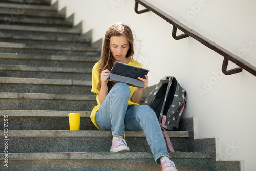 A girl on the street communicate on the gadget online. She sits on the steps. It's summer outside. Video chat. Communication online. Technology. Generation Z.