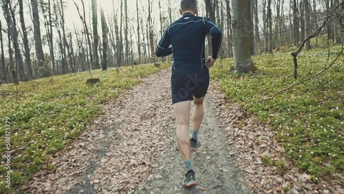 wide 4k slow motion shot of sporty man running in beautiful spring forest. Sport and wellness concept photo