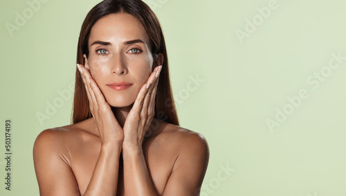 Anti-aging, spa and wellness. Adult woman with nourished, clear glowing skin, touching her soft beauty face and smiling, applies face lifting cream, white background