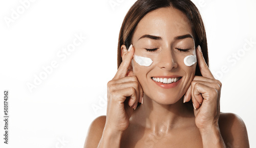 Fotografie, Obraz Cheerful middle aged, 40s years woman putting moisturizer cream on her face and laughing
