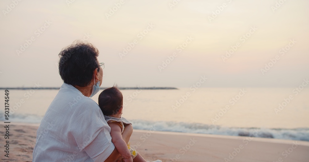happiness Asian family grandmother is keeping holding cute adorable newborn baby infant girl on her arms relaxing at seaside tropical beach sunrise morning during holiday vacation in Thailand happiness Asian family grandmother is keeping holding cute adorable newborn baby infant girl on her arms relaxing at seaside tropical beach sunrise morning during holiday vacation in Thailand