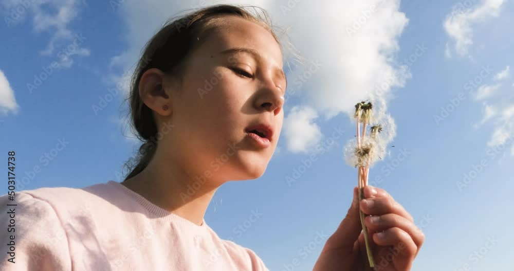 Portrait of adorable young girl blowing white dandelion against blue sky with clouds on spring day in nature. Close up view. 4K video footage. Slow motion. Portrait of adorable young girl blowing white dandelion against blue sky with clouds on spring day in nature. Close up view. 4K video footage. Slow motion.