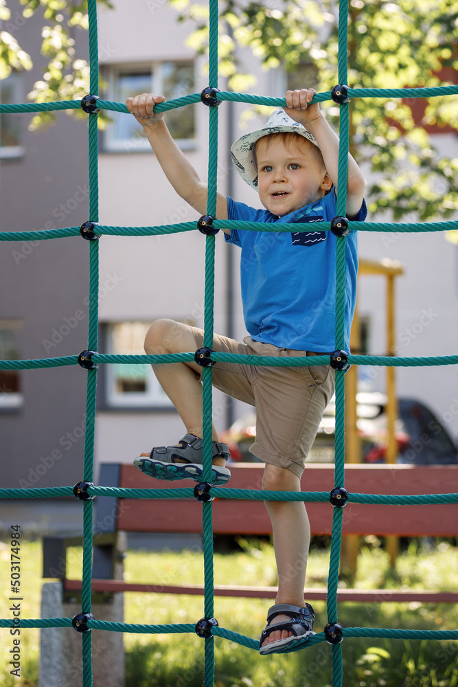 Child hanging on green rope net in city park. Child hanging on green rope net in city park.