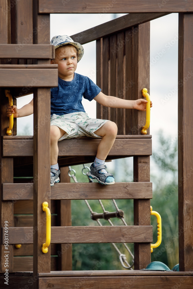 A cute little brave boy sitting at the top of the wooden playground. A cute little brave boy sitting at the top of the wooden playground.