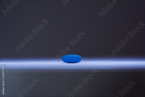Single blue pill illuminated by a single sharp beam photo