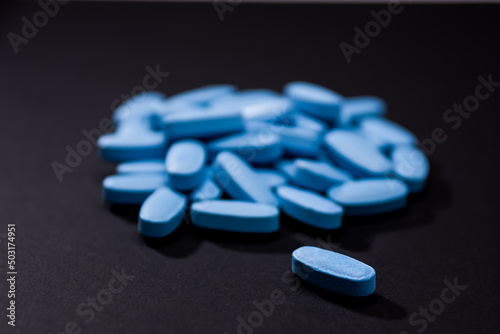 Blue pill in the foreground and blurry background heap of blue colored tablets photo